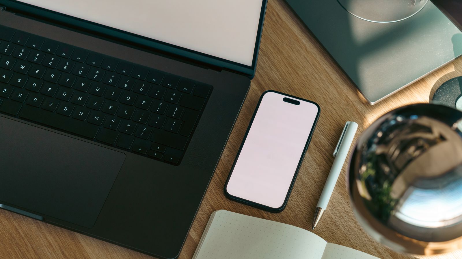 Laptop, phone, notebook, and pen laid out on a desk representing a solo marketing tool stack
